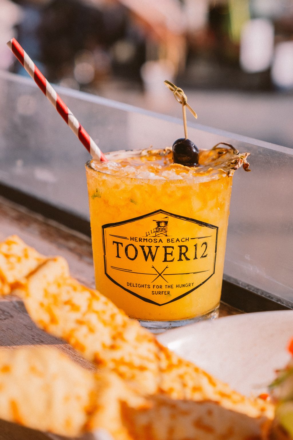 Orange cocktail over crushed ice in a Tower12-branded glass, garnished with a dark cherry and dried citrus.